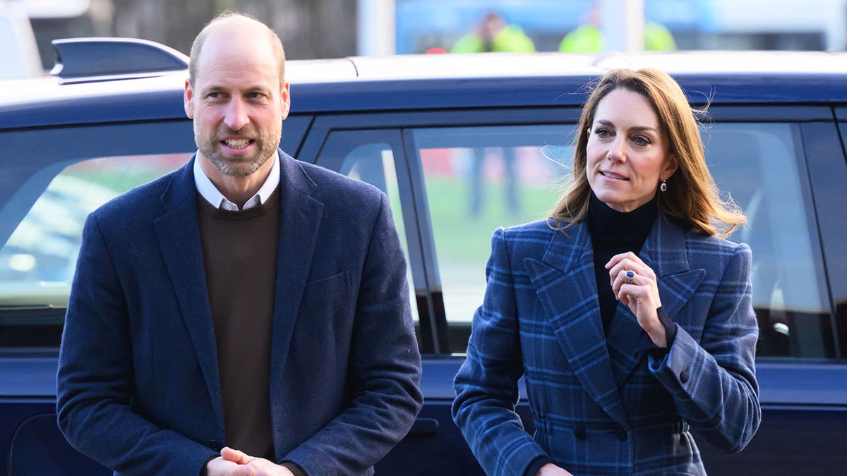 Prince William and Kate Middleton walking together in front of a car wearing matching blue attire.