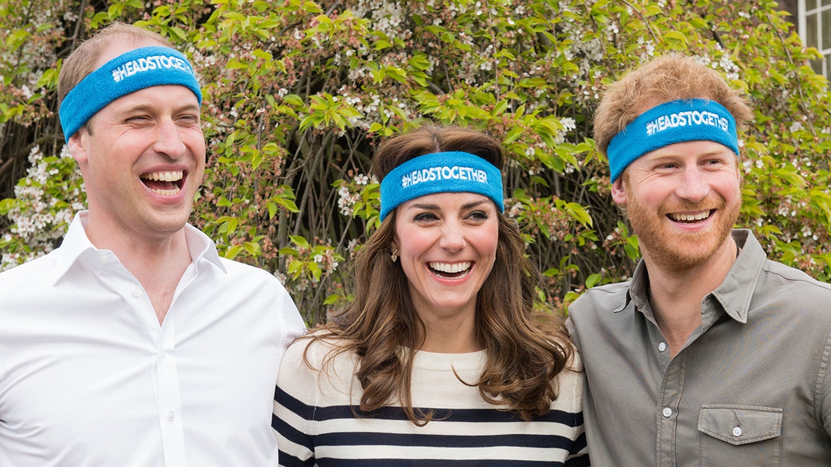 Prince William, Kate Middleton and Prince Harry smiling together wearing matching blue headbands.
