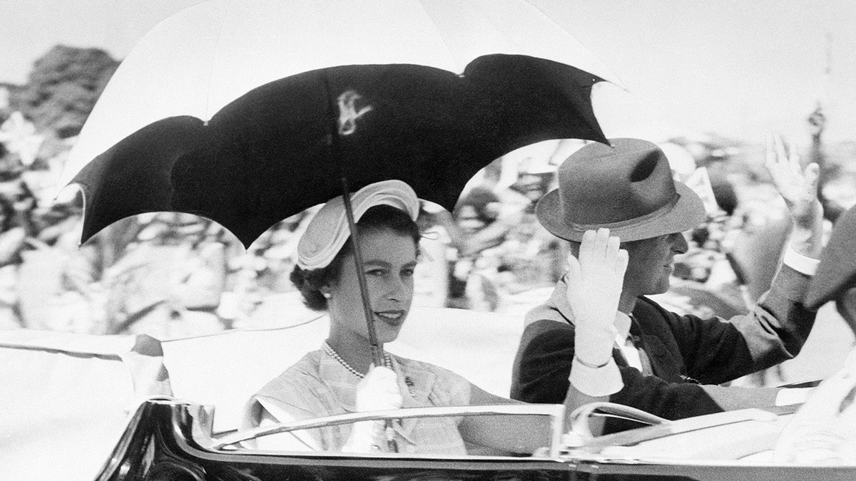 Queen Elizabeth holding an umbrella sitting next to Prince Philip in Australia.