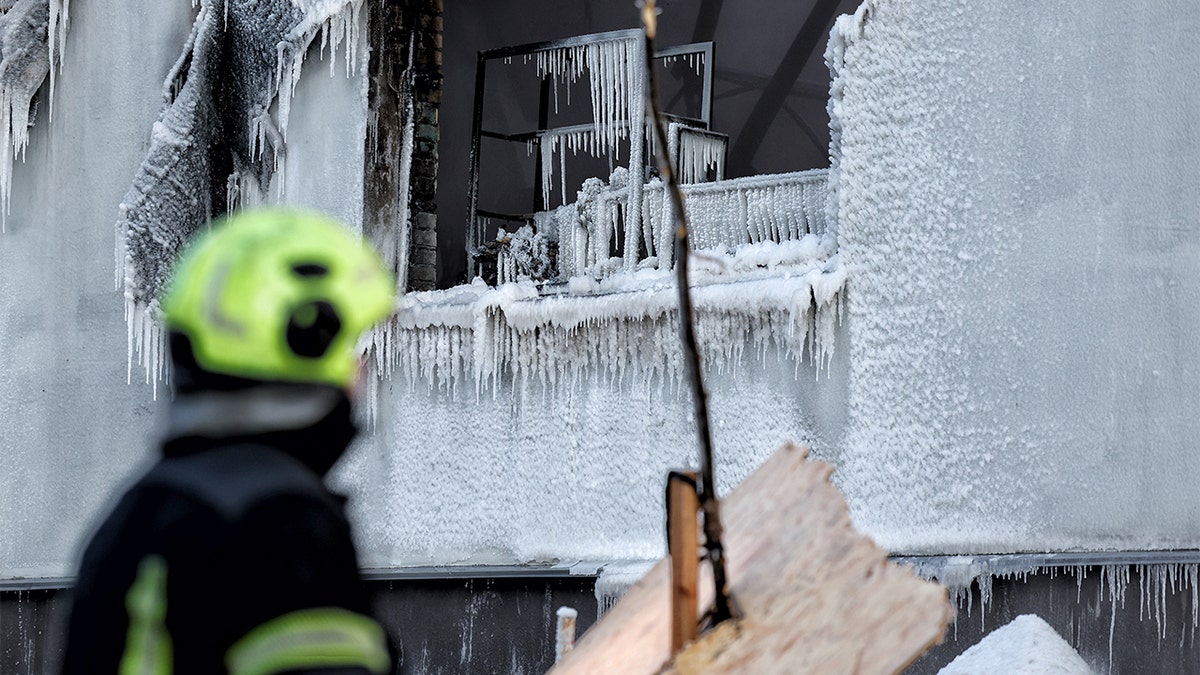 Firefighter works amid icy debris while putting out flames at a damaged structure following an overnight drone strike.