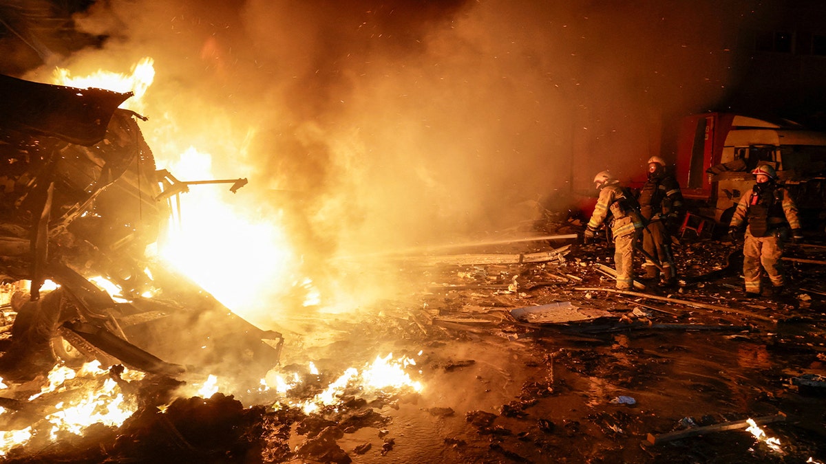 Firefighters respond to burning wreckage at a commercial facility following a missile strike.
