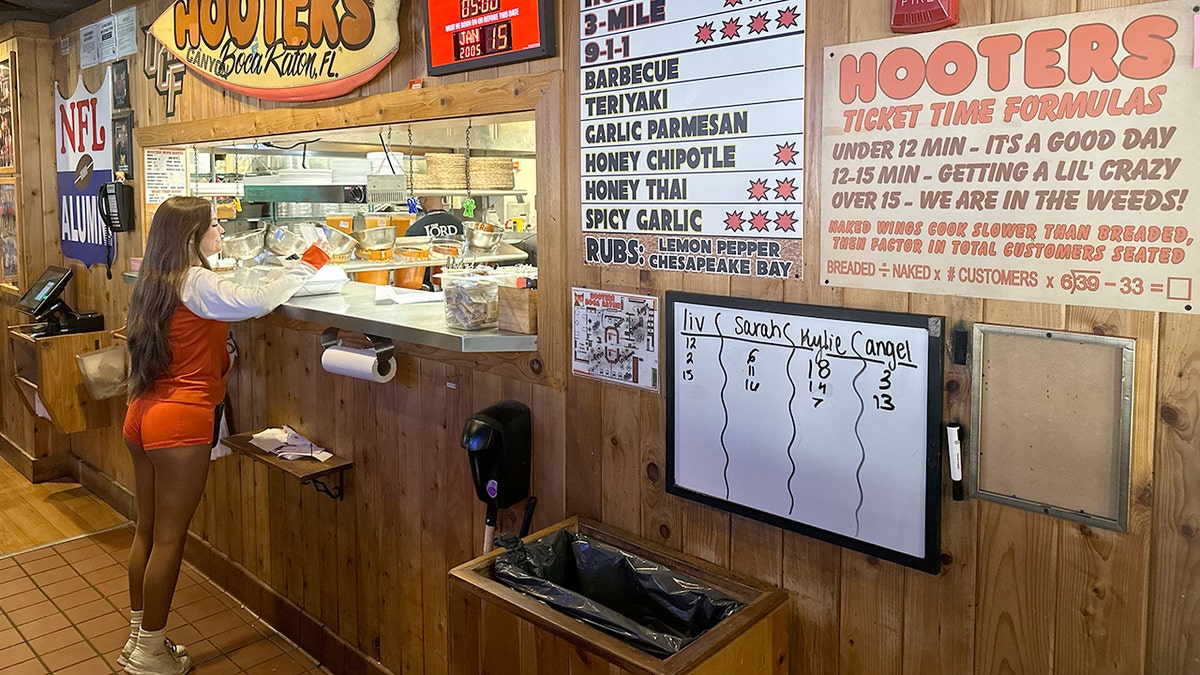 A Hooters waitress reviews a food order at the kitchen window in Boca Raton, Florida.