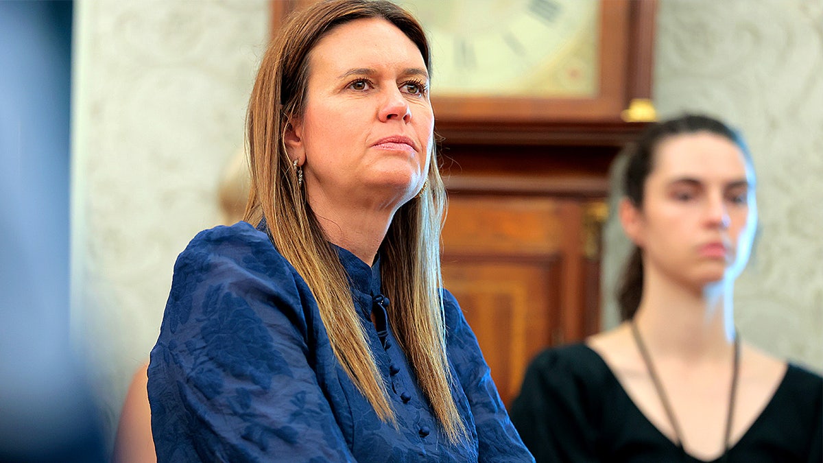 Sarah Huckabee Sanders stands inside the Oval Office during an event with President Donald Trump.