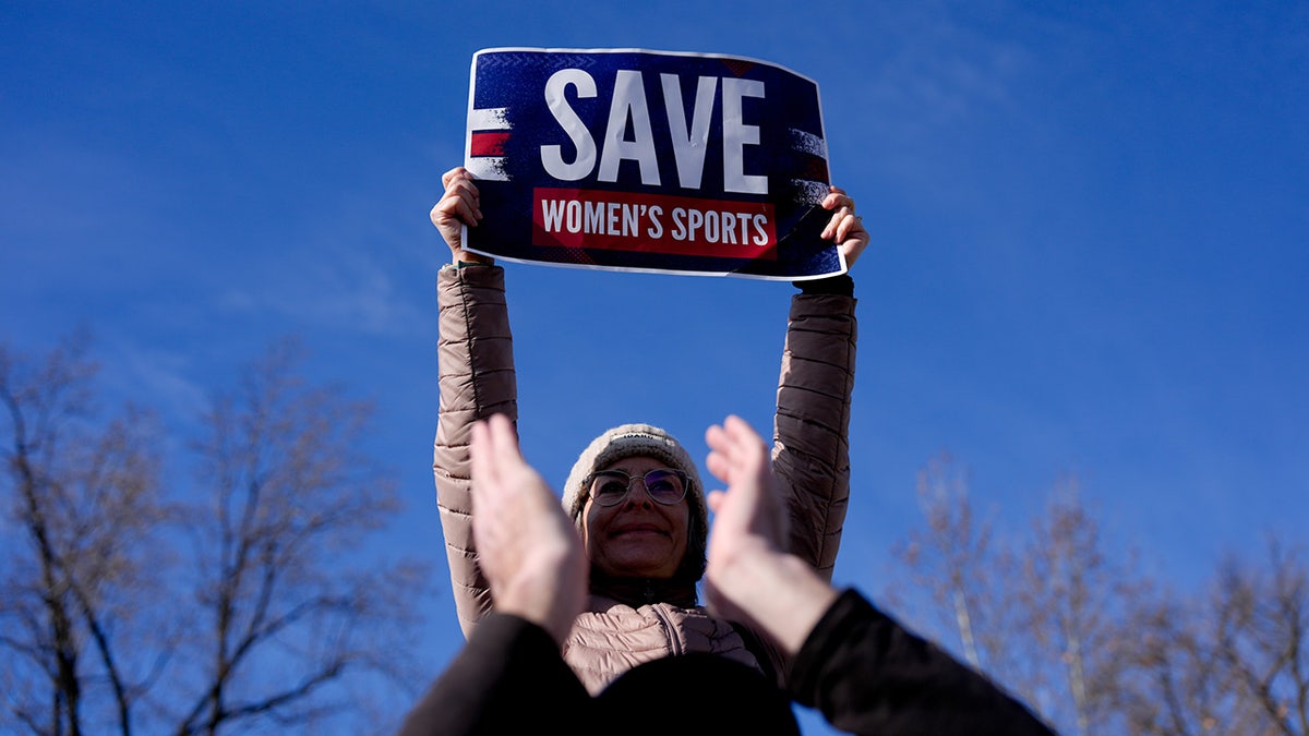 A woman holds a "save women's sports sign"