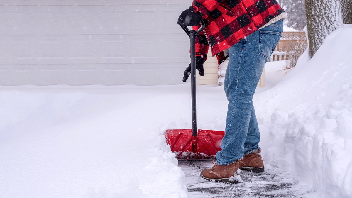 Hombre quitando la nieve de la entrada de tu casa después de una fuerte nevada.