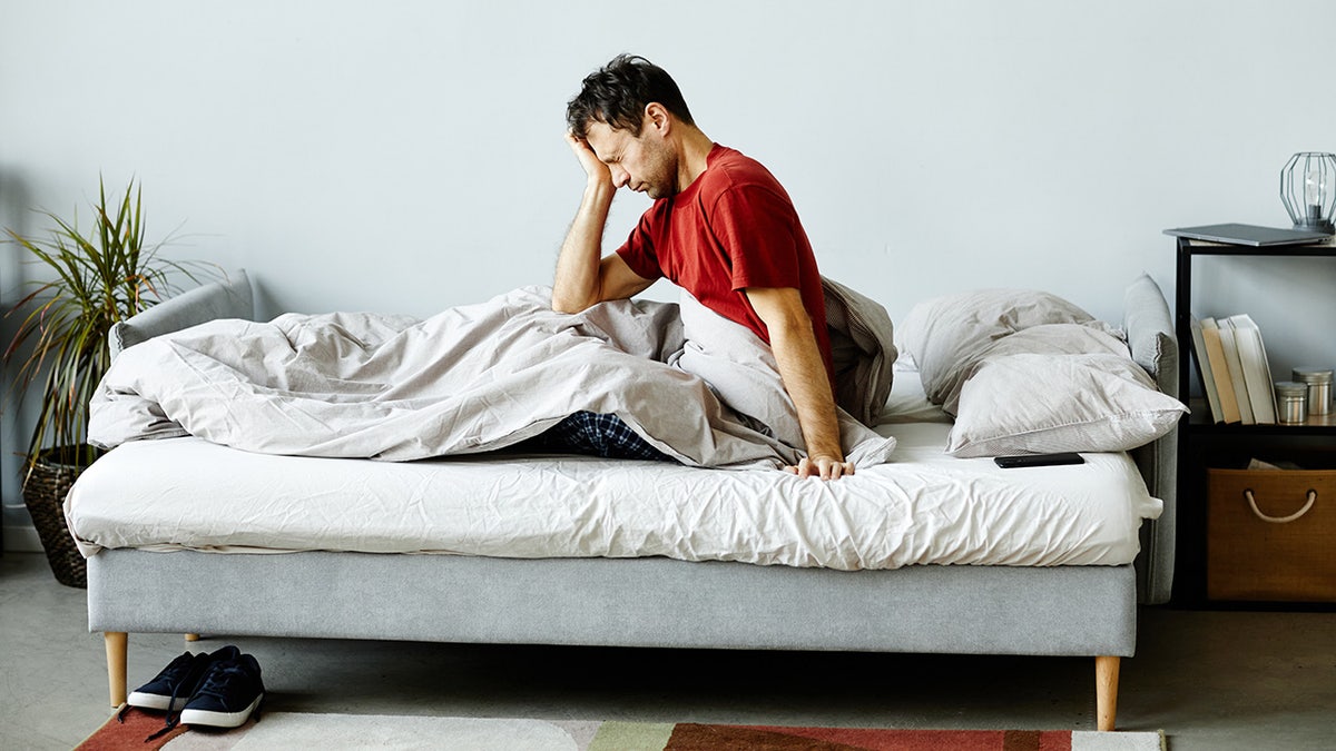 Exhausted middle-aged man sitting up in bed rubbing eyes.