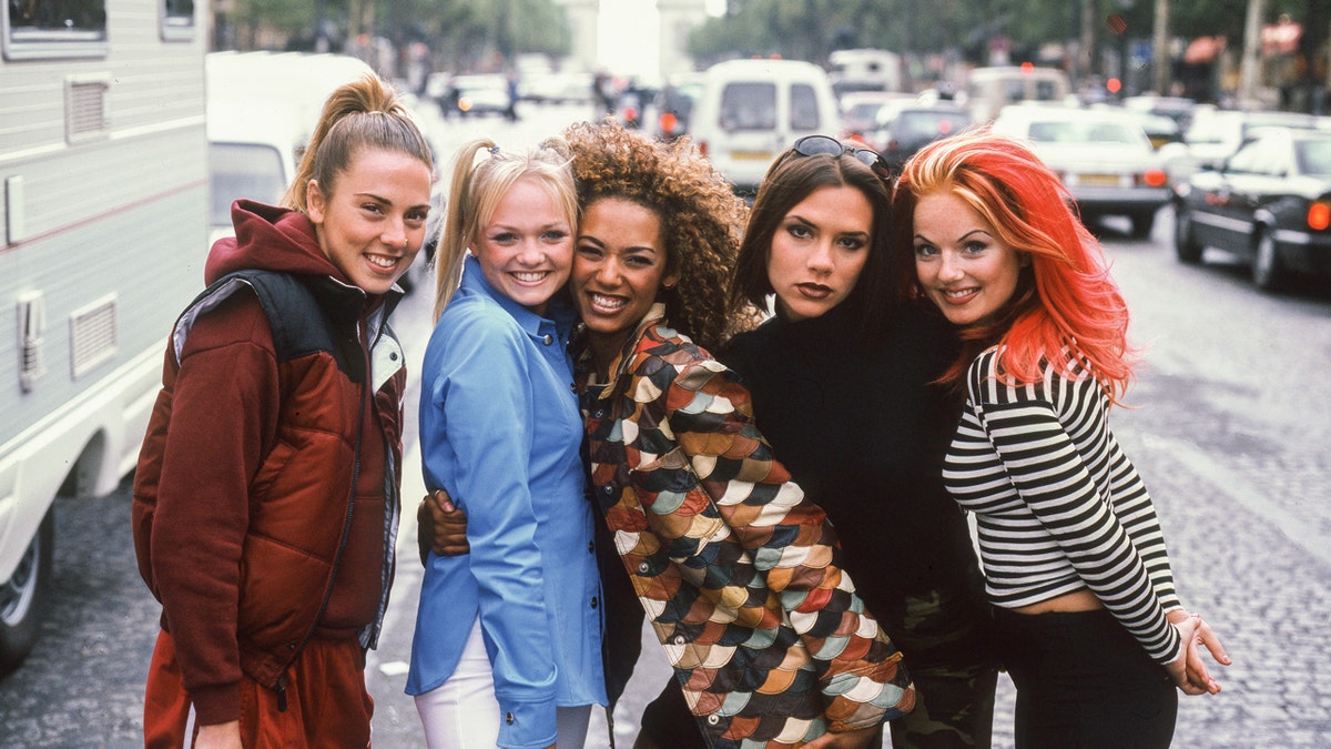 Las Spice Girls posan para una foto en una calle de la ciudad con el Arco del Triunfo al fondo.