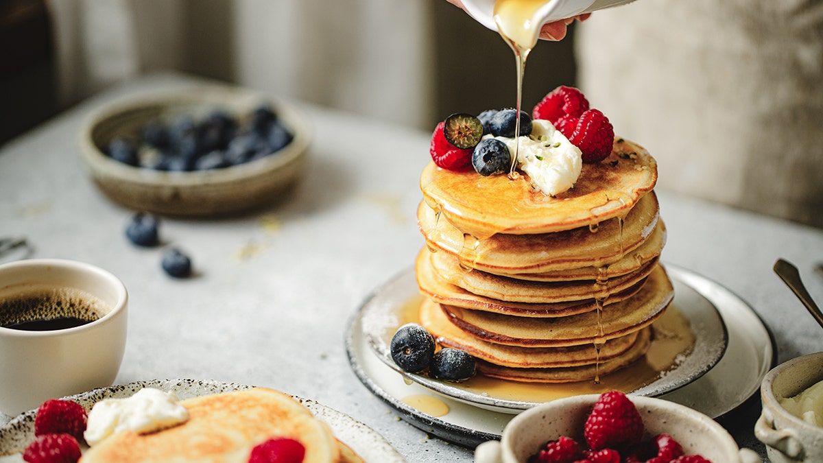 Stacked buttermilk pancakes with fruit and butter on the top.