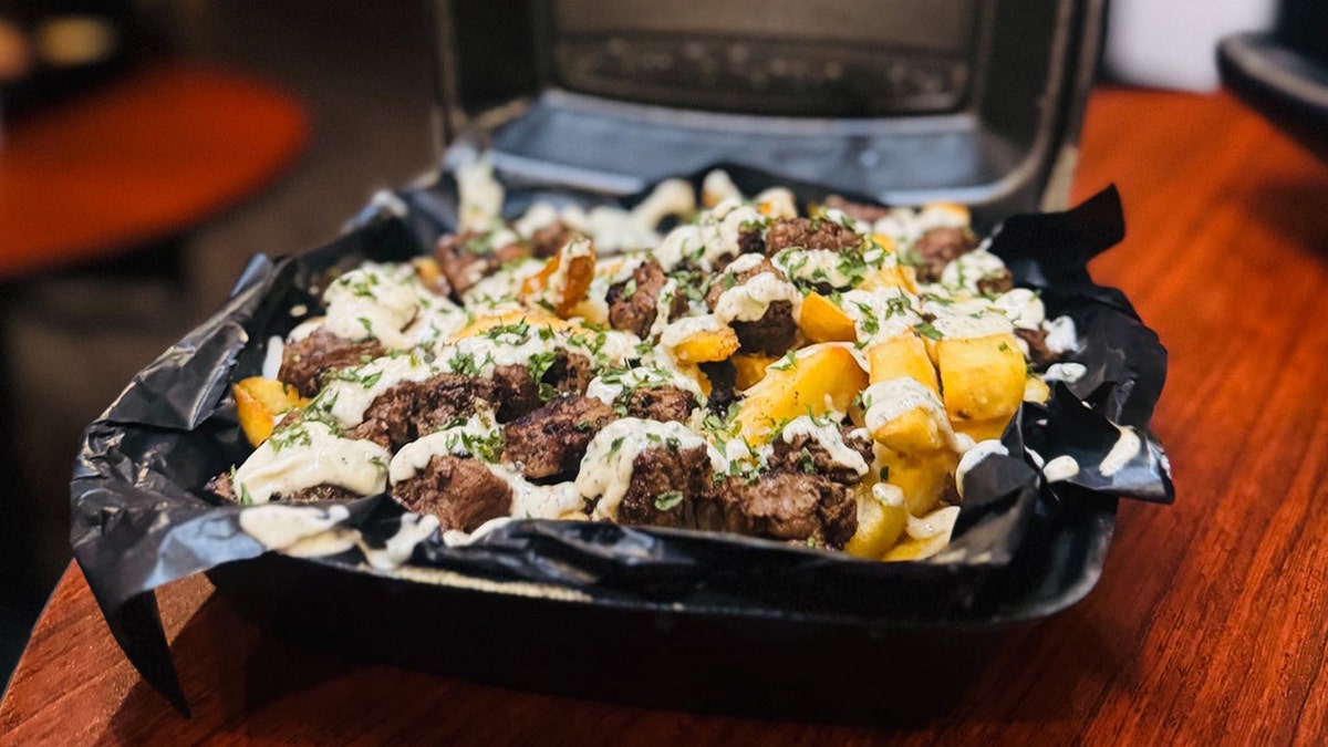 Fries loaded with Chopped Steak, Mozzarella, Green Pepper, Onion, Cheeze Wiz in a takeout container at The Last Word in Ohio.