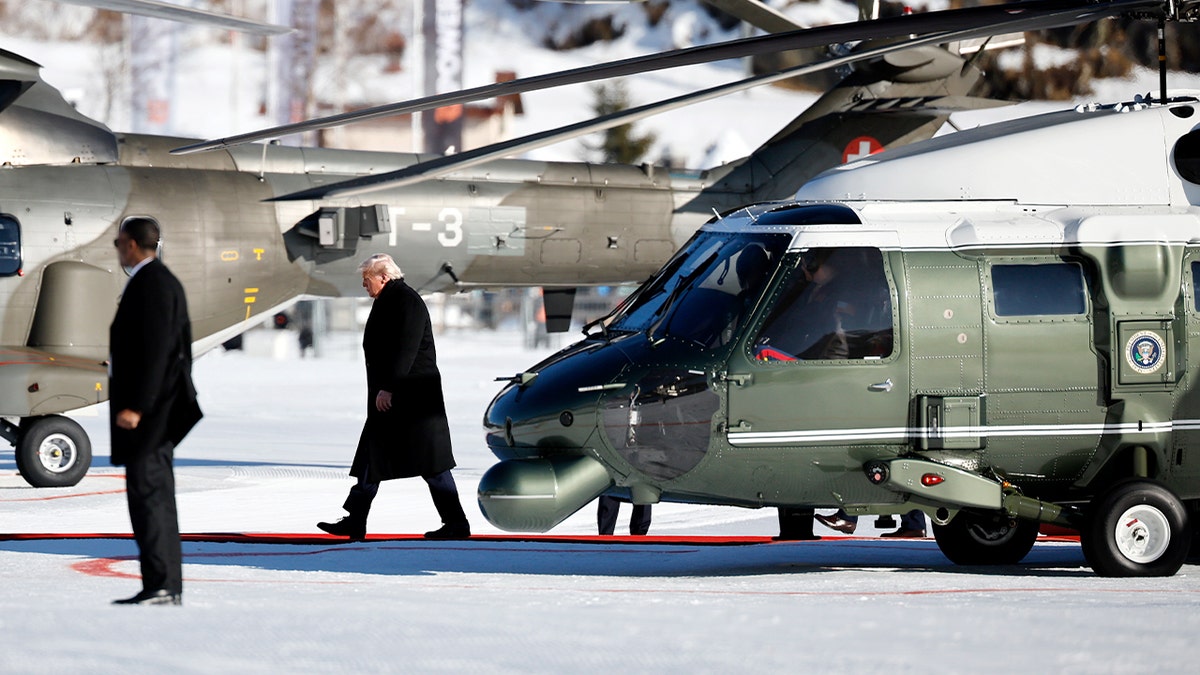 The U.S. president steps off a helicopter onto a snowy landing area.