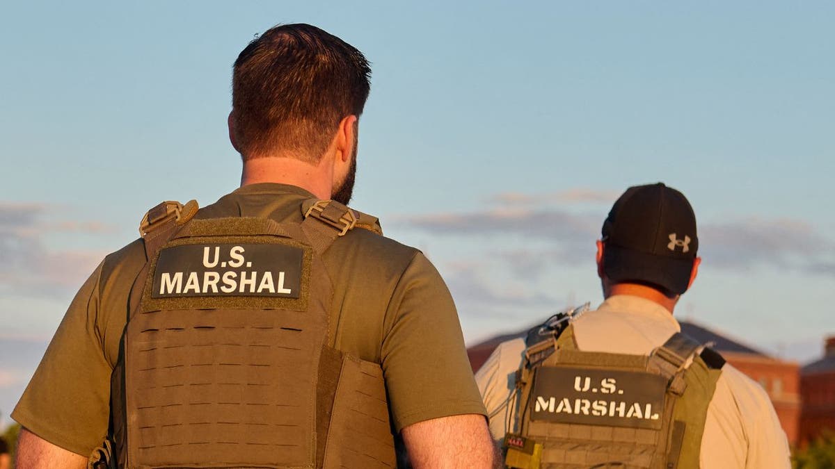 U.S. Marshals agents wearing tactical vests walk through a public park.