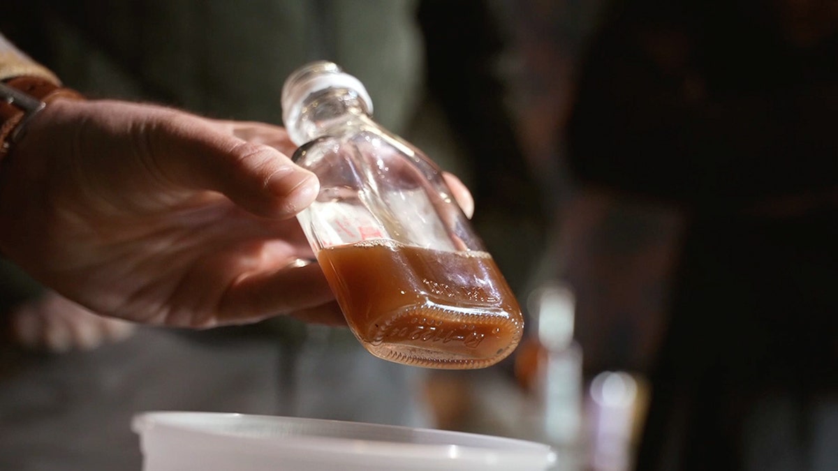 Distiller holds shot glass full of liquid
