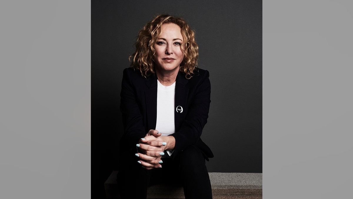 Virginia Madsen clasping her hands wearing a black blazer and a white shirt.
