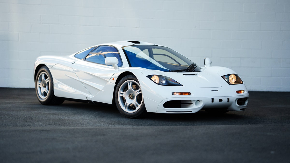 White McLaren F1 supercar parked outdoors, front three-quarter view with headlights on.