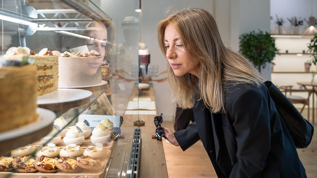 Donna che guarda torte e pasticcini all'interno di una vetrina da forno in vetro.