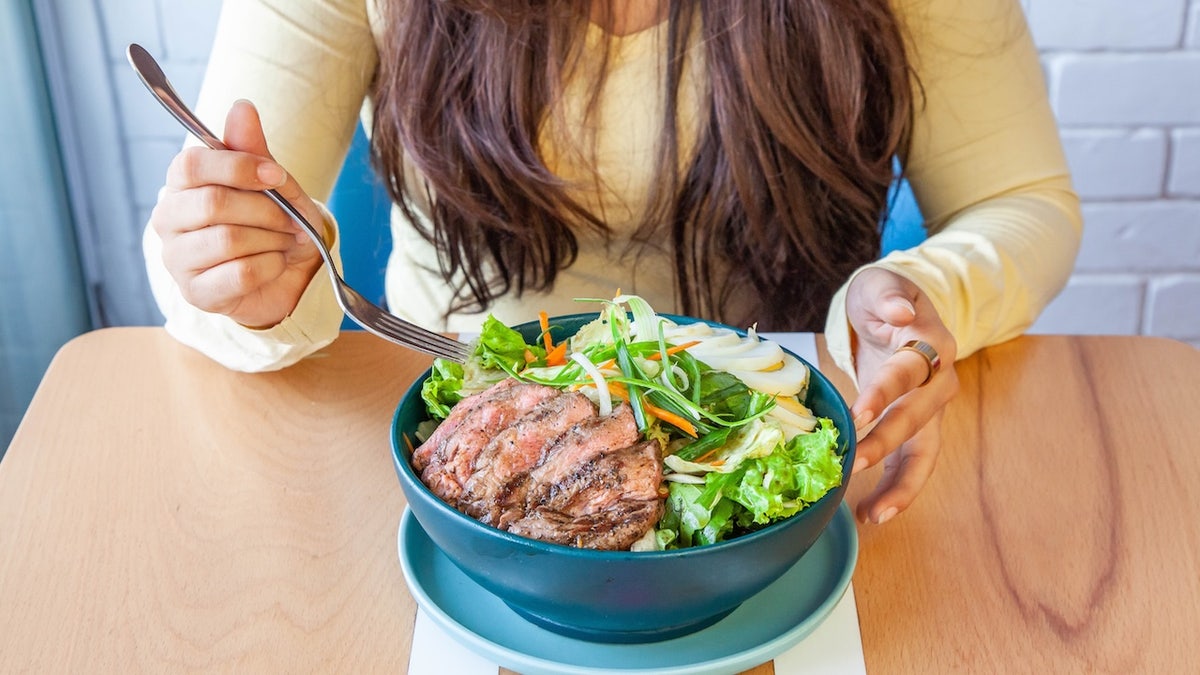 Mujer comiendo filete y ensalada