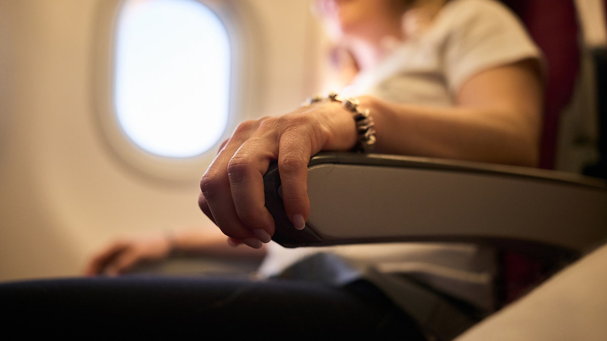 Airline passenger resting arm on seat armrest beside airplane window during flight.