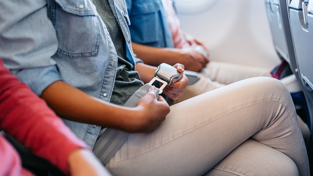 Passengers fastening seat belts while seated inside a commercial airplane cabin.