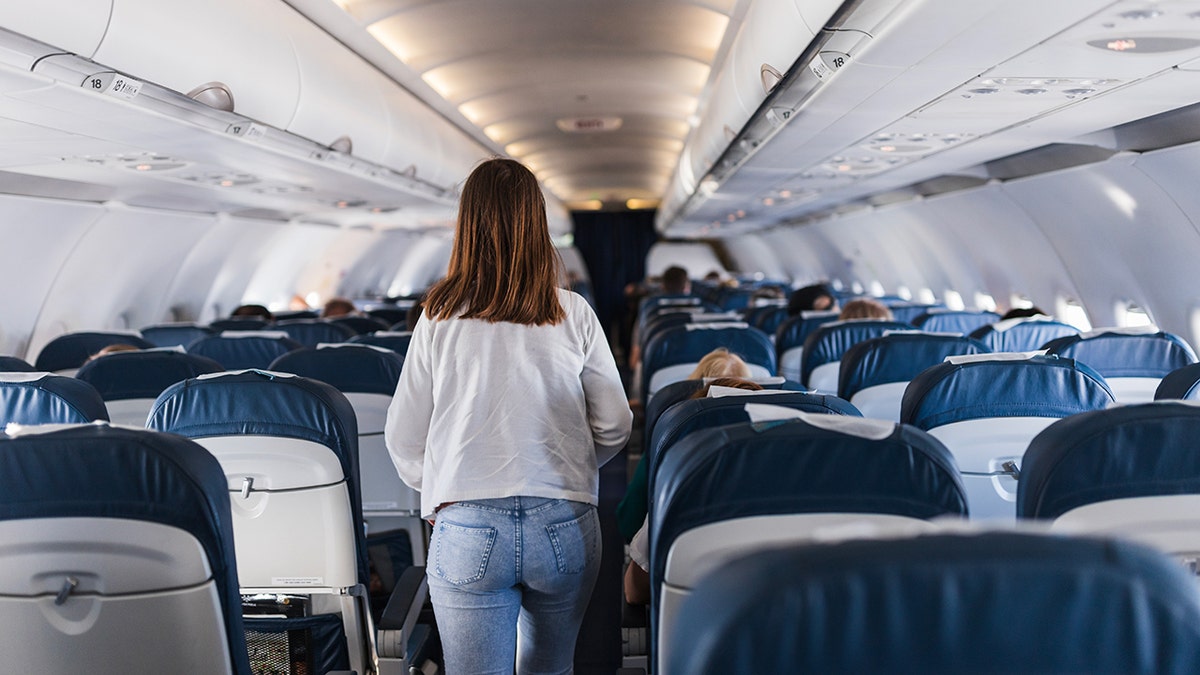 Passenger walks down the aisle of a commercial airplane cabin during a flight.