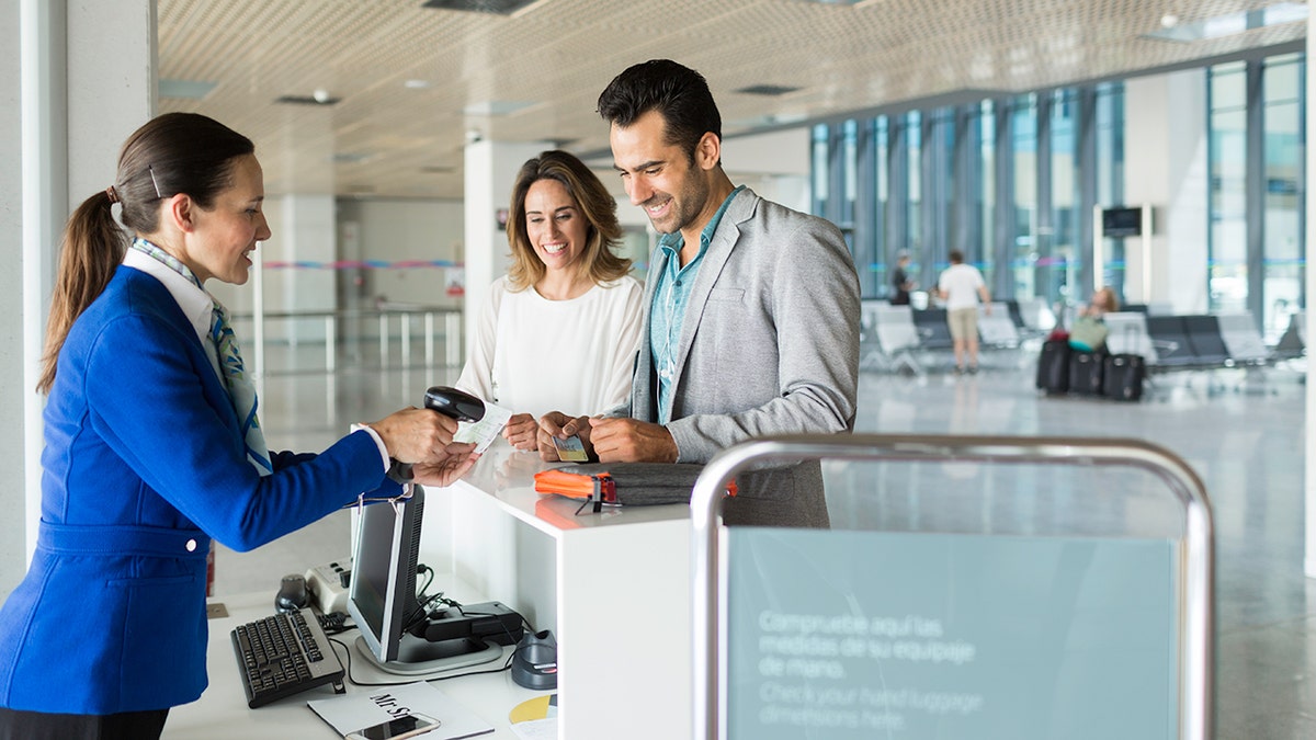 Airport check-in agent scanning boarding passes for a couple at a modern airport terminal counter.