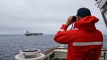 A member of the U.S. Coast Guard looking through binoculars at an oil tanker