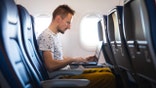 Man using a laptop while seated in an airplane cabin during a flight.