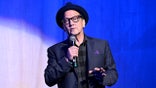 Rob Schneider holding a microphone on stage