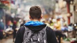 View of a young man from behind as he walks down a street wearing a backpack.