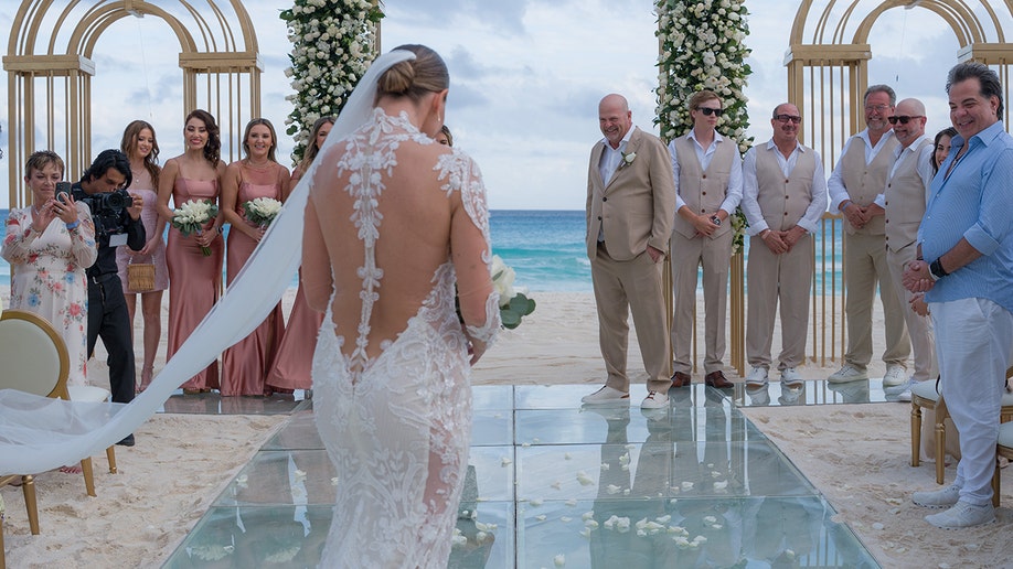 Rick Harrison stands at a beach altar in Cancún, Mexico, watching bride Agripina 