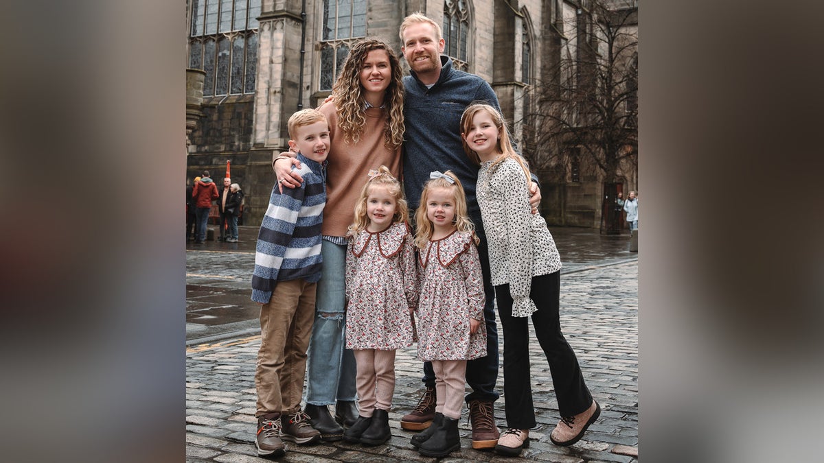 Ali Van De Graaff and her husband travel frequently with their four children smiling posing together outside church in Europe.