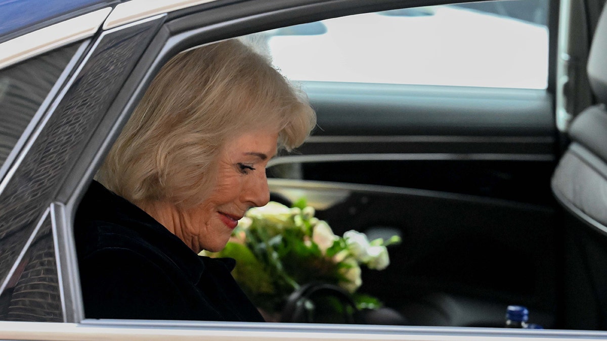 Queen Camilla looking down next to flowers inside a car.