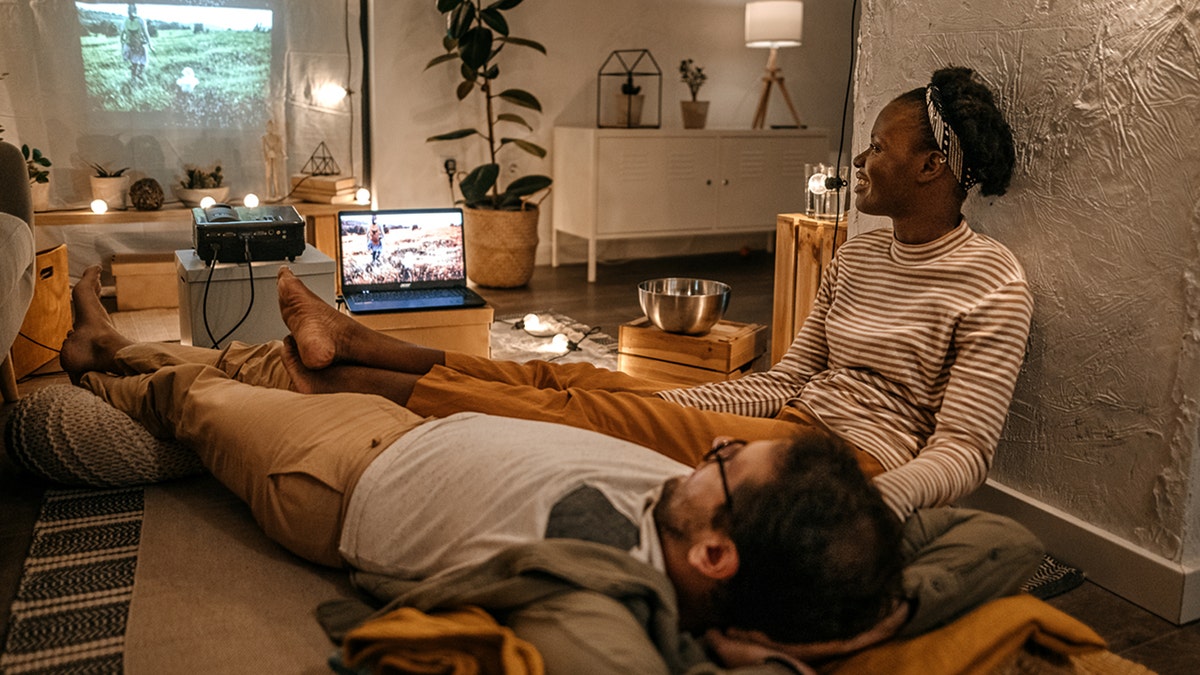 Young couple lying and sitting on floor watching a movie on their large projector screen at home