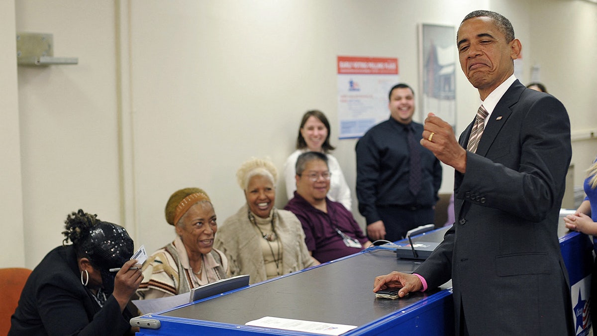 Then-President Barack Obama jokes with election worker Marie Holmes, left, who double-checked his photo on his driver's license as he signed in for early voting Oct. 25, 2012, at the Martin Luther King Community Center in Chicago.