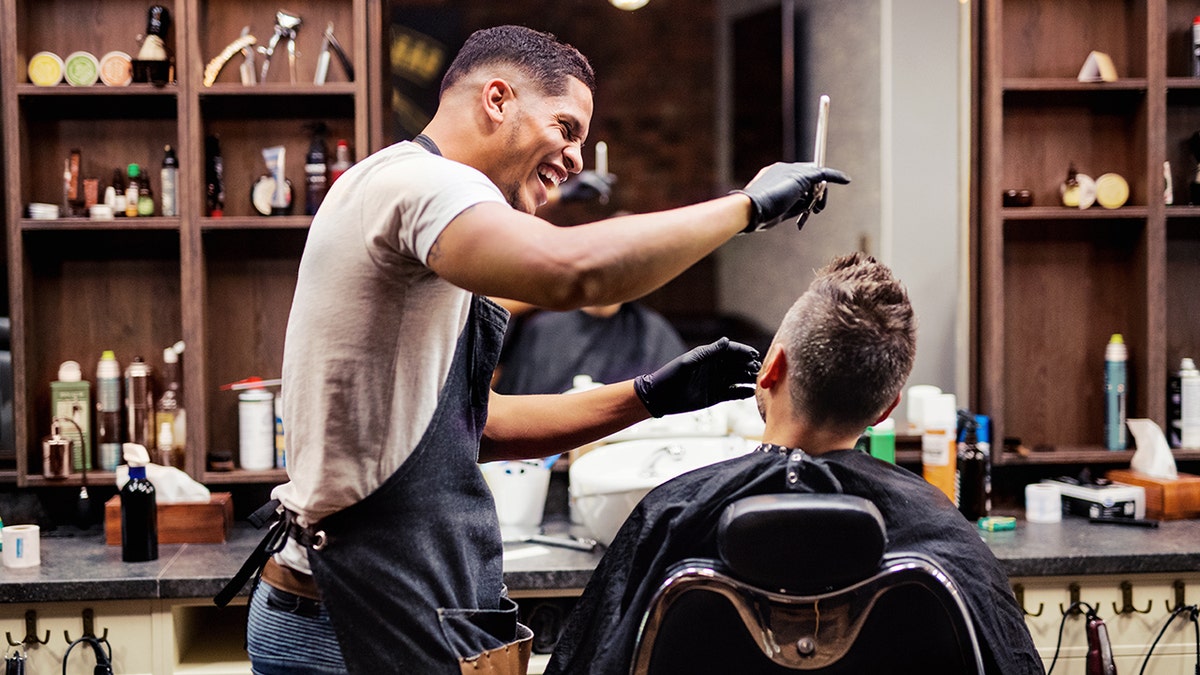 Barber smiles as he cuts young man's hair.