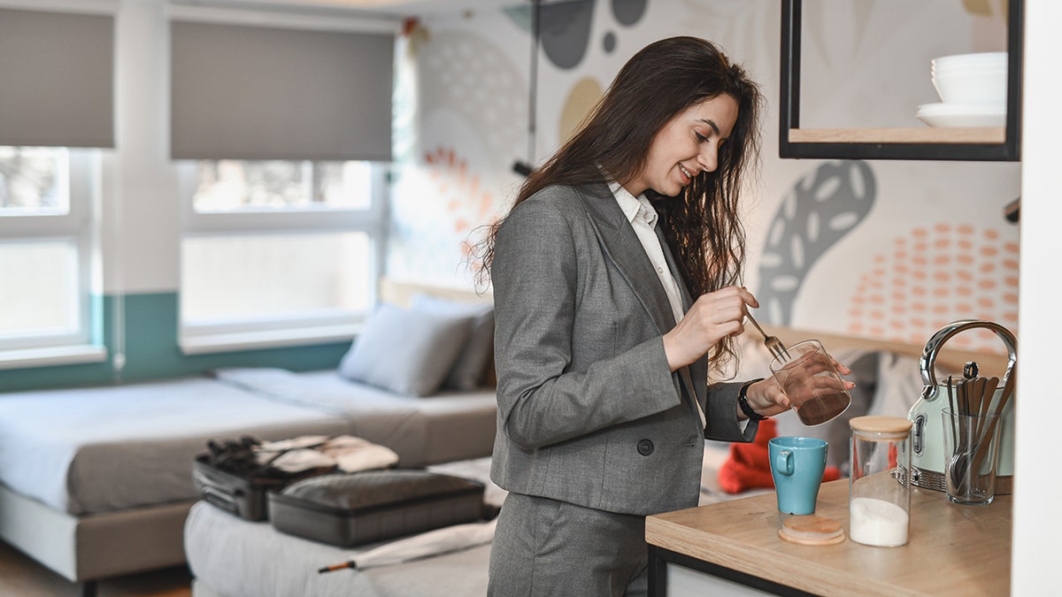 Businesswoman in hotel room making coffee while preparing for work trip.