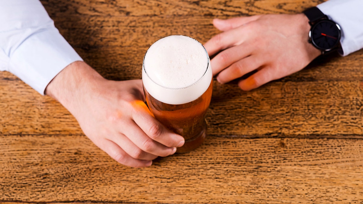 A businessman holds a beer mug on a counter.