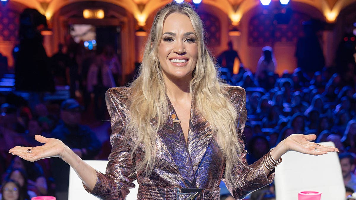 Carrie Underwood poses in front of the American Idol audience while shrugging 