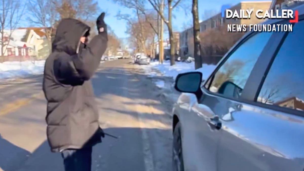 A person in a winter jacket approaches a vehicle on a snowy residential street in Minneapolis