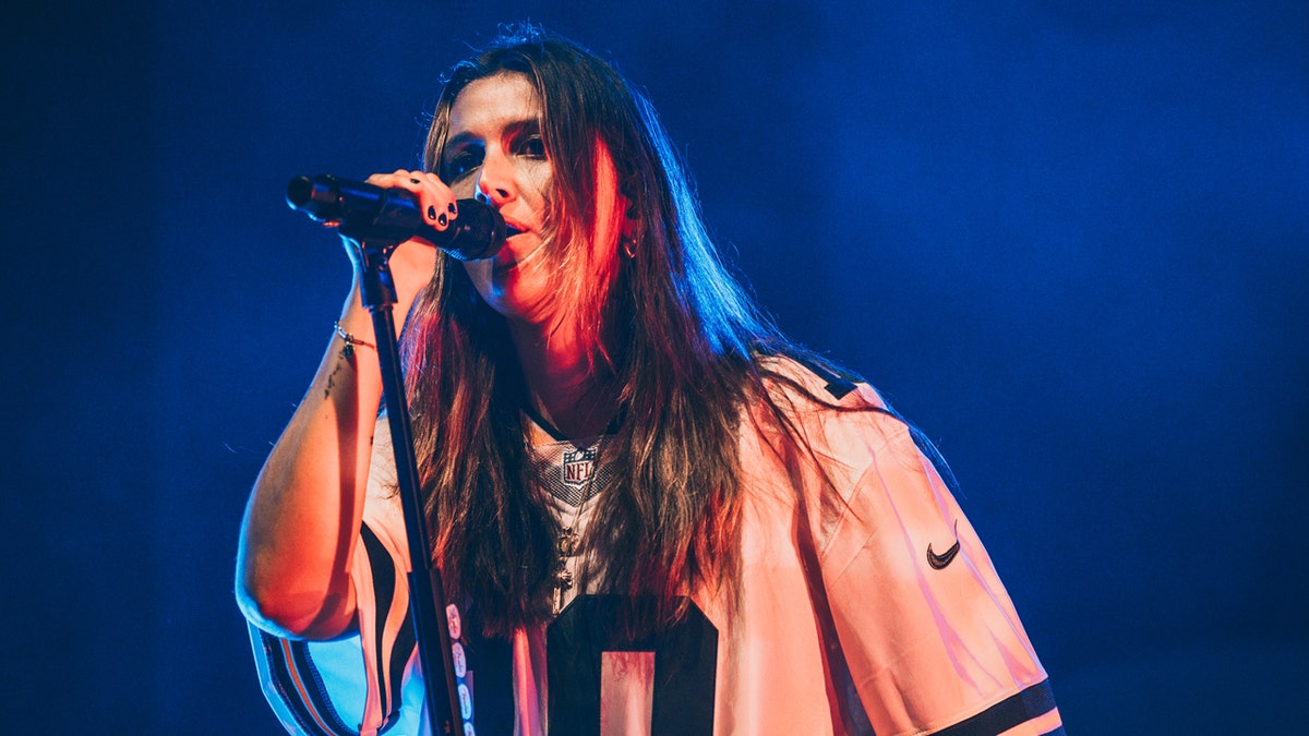 Chelsea Cutler singing into a microphone while performing on a stage.