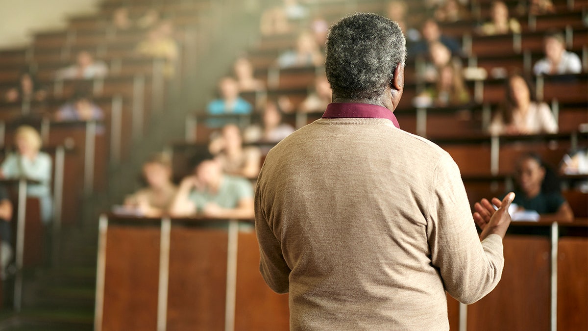 A professor speaks to a large group of students during a class in a university lecture hall.