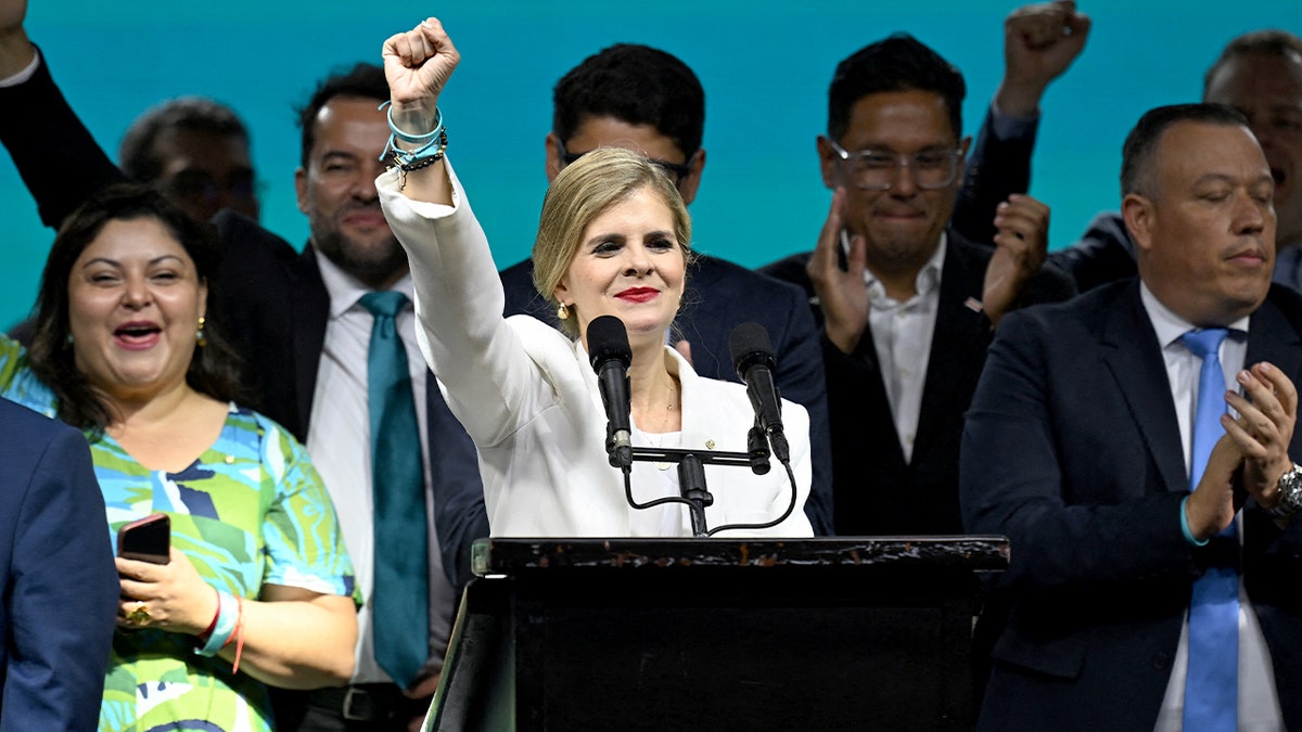 A woman raises her hand toward an applauding crowd inside a hotel ballroom during a post-election event.
