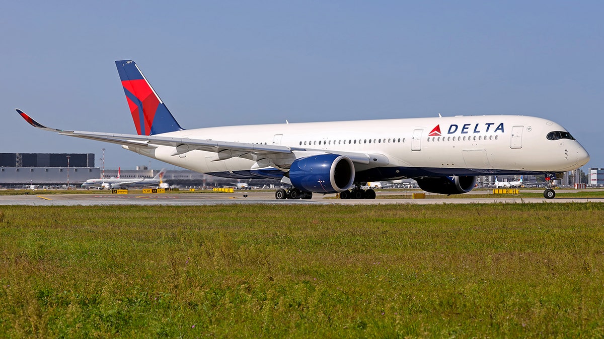 Delta Air Lines Airbus A350 widebody aircraft taxiing on a runway at an airport, with blue engines and red-and-blue tail livery visible against a clear sky.