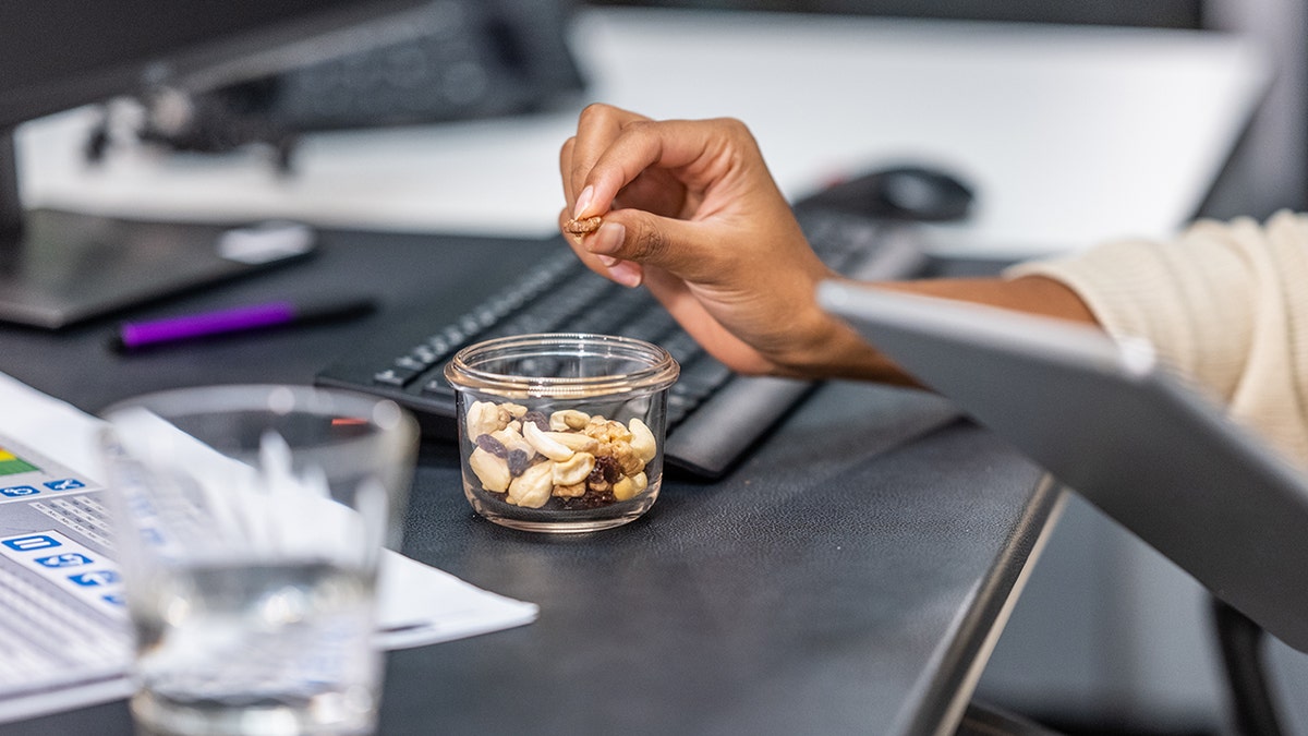 Close-up photo of a woman's hands holding nuts and raisins while using a digital tablet.
