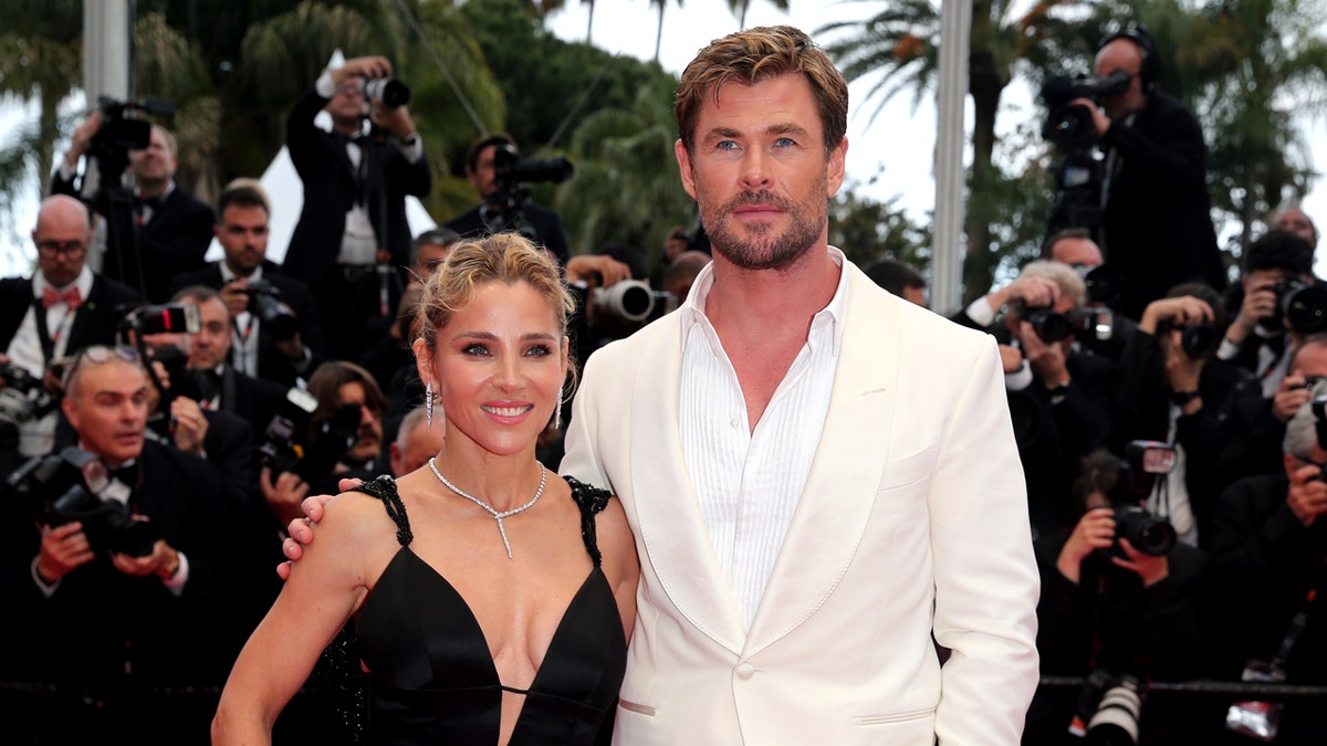 Elsa Pataky and Chris Hemsworth standing together on a red carpet in front of a branded backdrop.