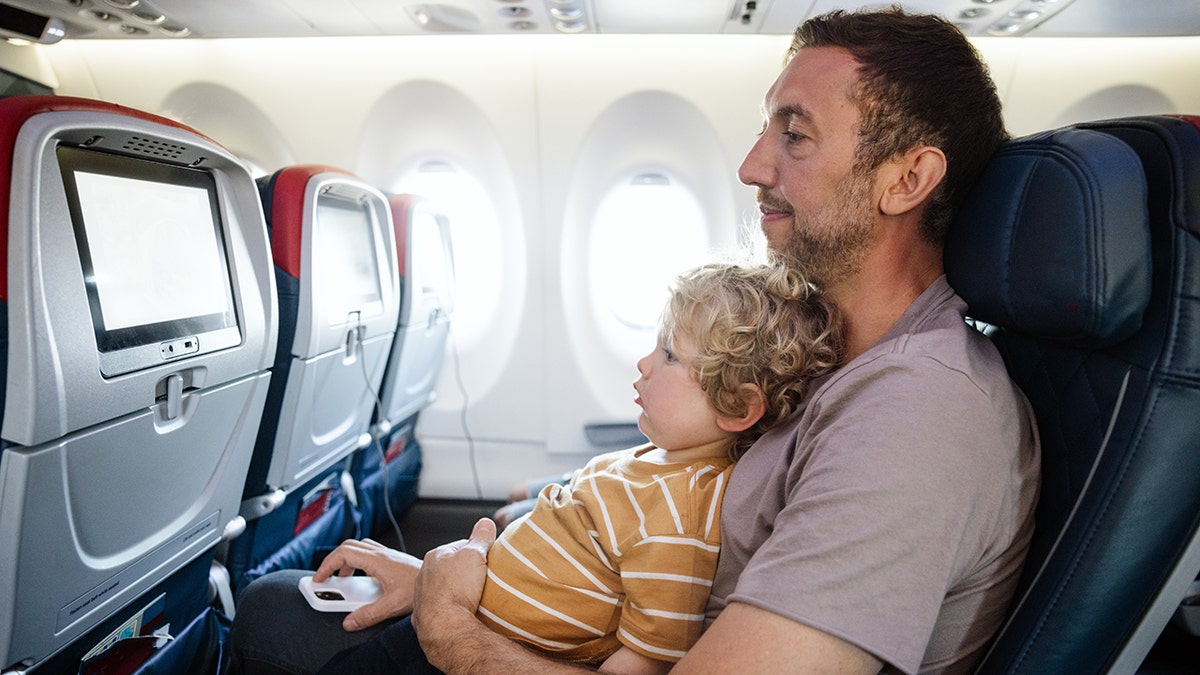 Padre e figlio seduti insieme sull'aereo guardando lo schermo dell'intrattenimento a bordo.