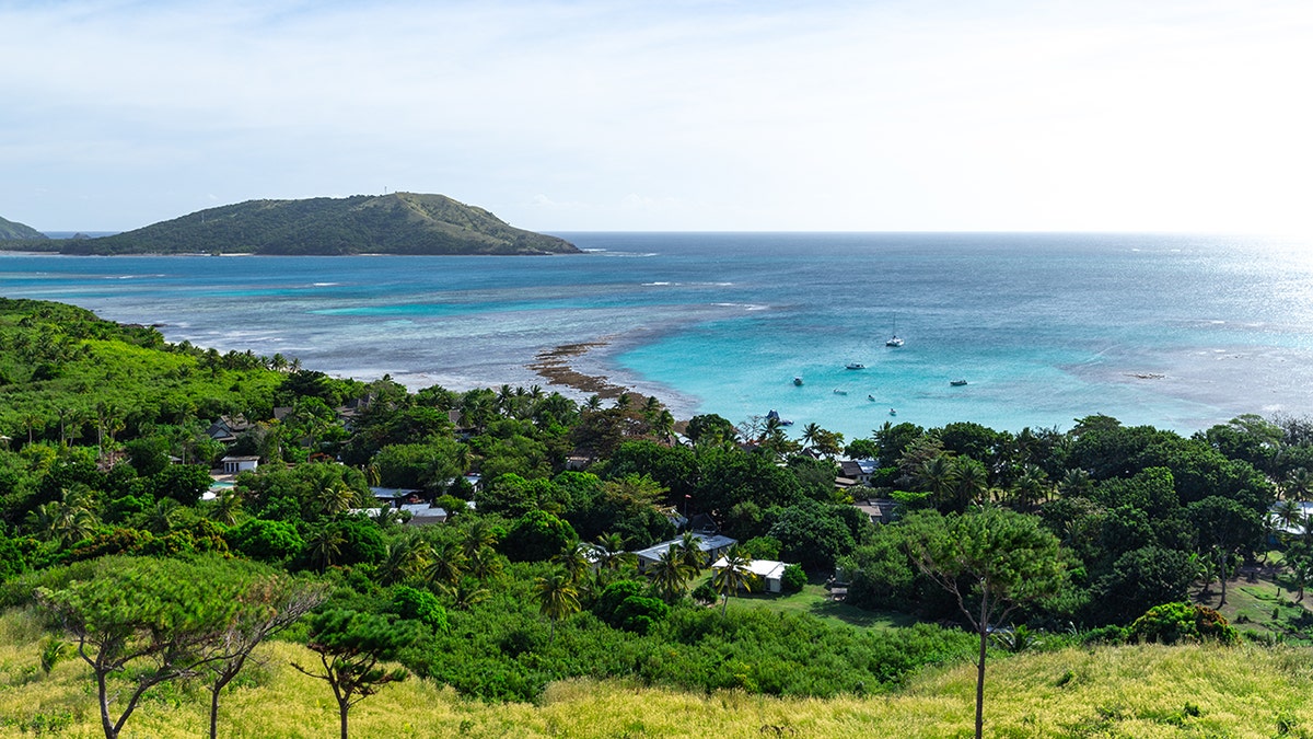 Panoramic view of tropical coastline in Fiji with turquoise ocean, lush greenery and anchored boats.