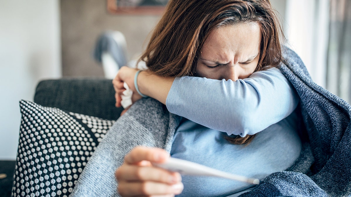 Woman coughing into sleeve checking symptoms
