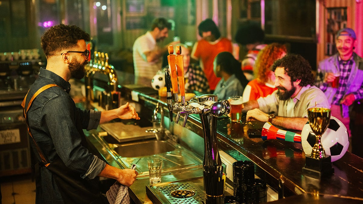 Young people hanging out at sports bar, chatting with friendly bartender.