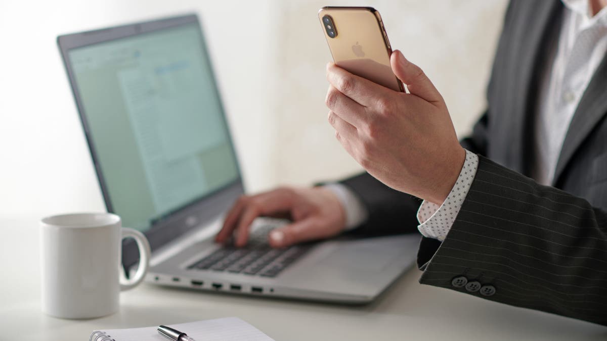 Man holding phone while typing on computer.