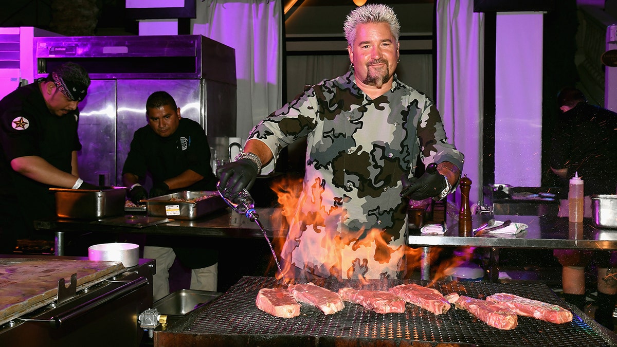 Guy Fieri grilling steaks behind a fiery grill in Vegas.